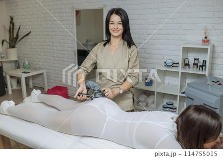 Woman in special white suit getting anti cellulite massage in a spa salon. LPG, and body contouring treatment in clinic.Reset body weight with LPG massage 114755015