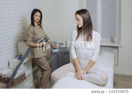 Woman in special white suit getting anti cellulite massage in a spa salon. LPG, and body contouring treatment in clinic.Reset body weight with LPG massage 114755075