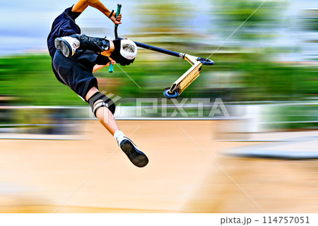 Young man practicing Scootering (Freestyle Scootering) in the new SkatePark in the central park of Igualada, Barcelona, Spain. blurred background	 114757051