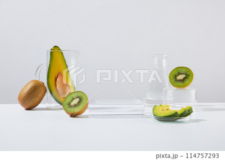 Avocado and kiwi theme photo on white background in laboratory layout with several lab glass utensils, a blank glass podium in center for showing product. Frontal shot with displaying space Avocado and kiwi theme photo on white background in laboratory layout with several lab glass utensils, a blank glass podium in center for showing product. Frontal shot with displaying space 114757293