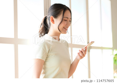 窓際に立ってスマホを見る若い女性 窓際に立ってスマホを見る若い女性 114757605
