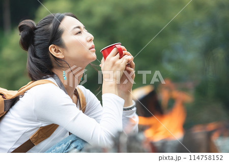 焚き火の横でコーヒーを飲む女性 114758152