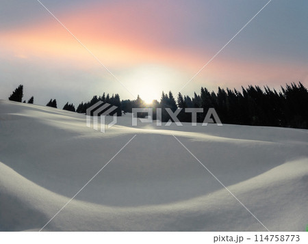 Dawn in the winter mountains of Central Asia. The morning sun peeks out from behind the mountain, illuminating the snow-covered slope. 114758773
