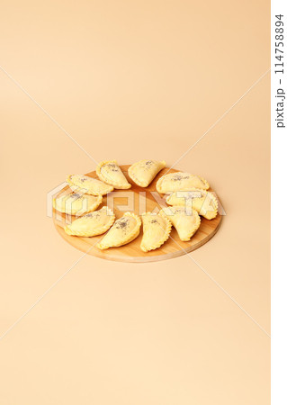 Raw samosas on a wooden round board. Traditional Central Asian cuisine, frozen semi-finished products, copy space. 114758894