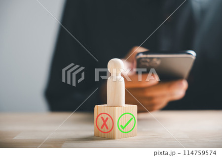 Businessman using smartphones selects right or wrong symbols on wooden block for a yes or no decision-making. Communication of choice and progress. Think With Yes Or No Choice. 114759574