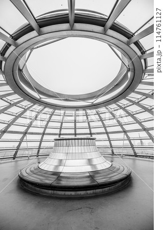 Inside view of the Reichstag glass dome in Berlin showing the top part with circular bench under the glass rooftop and steel framework. Berlin, Germany. Black and white image. 114761127