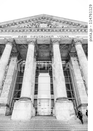 The monochrome facade of the Reichstag building, showcasing its iconic pillars and inscription: Dem Deutschen Volke. The seat of the German Bundestag, Berlin, Germany. Black and white image. The monochrome facade of the Reichstag building, showcasing its iconic pillars and inscription: Dem Deutschen Volke. The seat of the German Bundestag, Berlin, Germany. Black and white image. 114761129