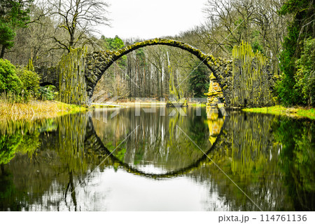 Rakotz Bridge arcs over calm waters, creating a perfect circular reflection amid tranquil greenery. Germany 114761136