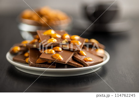 Broken chocolate bar with almonds on plate on black table. 114762245