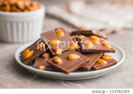 Broken chocolate bar with almonds on plate on kitchen table. 114762265