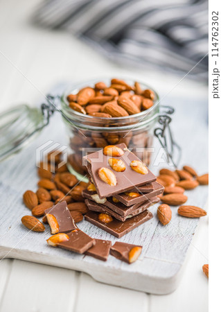 Broken chocolate bar with almonds on kitchen table. 114762302