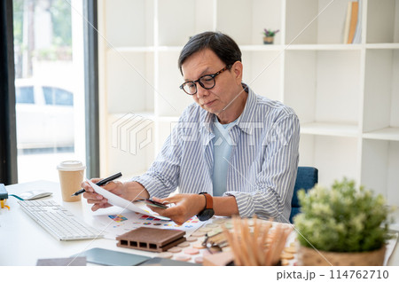A satisfied senior Asian male interior designer is checking the building material on samples. 114762710