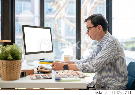 An experienced Asian male interior designer or architect is working on his project in the office. 114762711