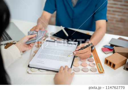 A client is signing a house building insurance contract and paying money to her contractor. A client is signing a house building insurance contract and paying money to her contractor. 114762770