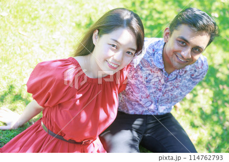 芝生に座り会話を楽しむ国際カップル 芝生に座り会話を楽しむ国際カップル 114762793