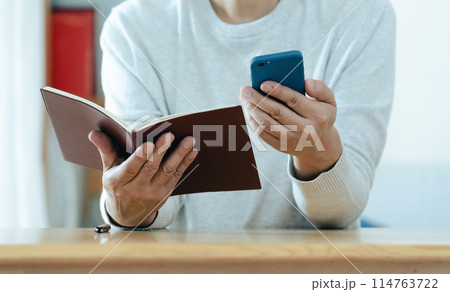 スマホと手帳をチェックするミドル男性 114763722