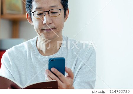 スマホと手帳をチェックするミドル男性 114763729