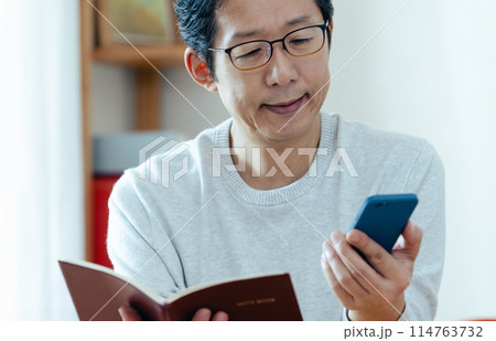 スマホと手帳をチェックするミドル男性 114763732
