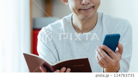 スマホと手帳をチェックするミドル男性 スマホと手帳をチェックするミドル男性 114763735