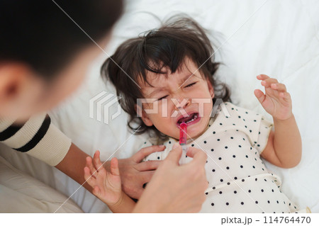 mother feeding liquid medicine to baby girl by syringe. sick crying toddler 114764470