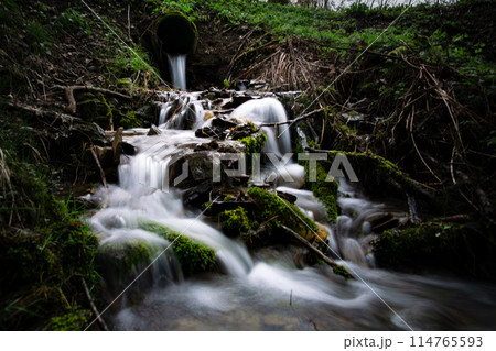 In the woods, a pipe releases water forming a beautiful waterfall 114765593