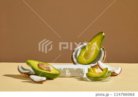 A light color table top displaying fresh fruits ingredient for manufacturing organic beauty care product consist of avocado and coconut with a blank white podium in center. Vacant space for design A light color table top displaying fresh fruits ingredient for manufacturing organic beauty care product consist of avocado and coconut with a blank white podium in center. Vacant space for design 114766068