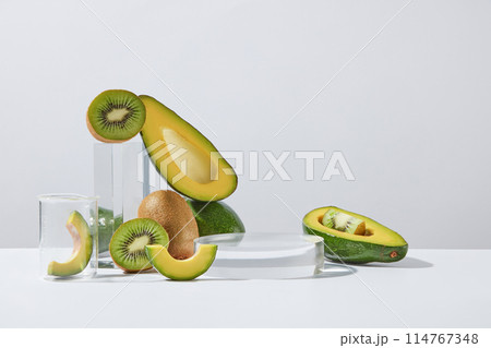 Glass podium in round shaped decorated with avocado and kiwi cut in some slices and halves. White background. Laboratory experience and research concept 114767348