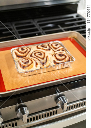 Just out of the oven, cinnamon rolls cool on a silicone baking mat, their icing glistening under the kitchen lights. Just out of the oven, cinnamon rolls cool on a silicone baking mat, their icing glistening under the kitchen lights. 114770454