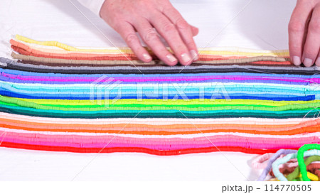 Hands touch a neatly organized rainbow of colorful, coiled clay bead strands against a contrasting white surface. 114770505
