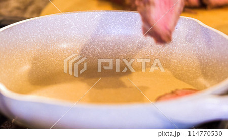 Tongs turning succulent medium-rare steak strips in a speckled ceramic skillet. 114770530