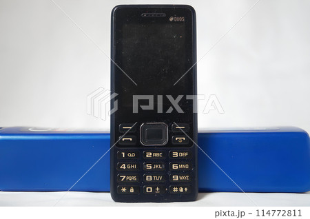 A black flip phone sits on a blue object A black flip phone sits on a blue object 114772811