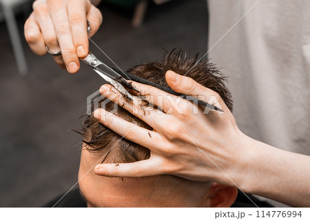 Barber uses scissors and comb to style the mans hair at the barbershop 114776994