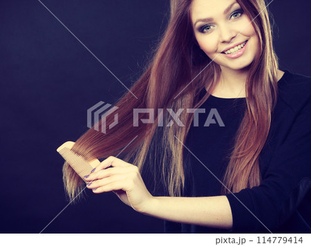Long haired woman combing her hair. 114779414