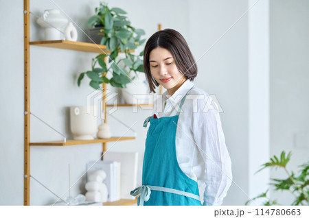 部屋でエプロンを付けた若い主婦 部屋でエプロンを付けた若い主婦 114780663