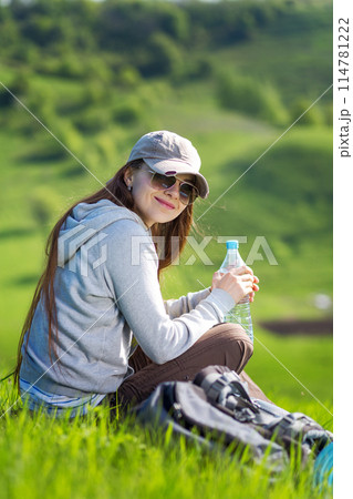 Young hiking woman taking a rest at green hill for rehydration 114781222