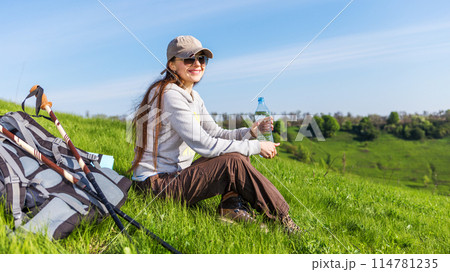 Young hiking woman taking a rest at green hill for rehydration 114781235