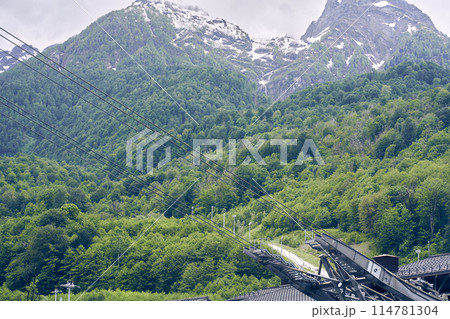 The mechanisms of the cable car are high against the background of snow-capped mountains. The concept of active recreation and tourism. A beautiful landscape with space to copy. High quality photo 114781304