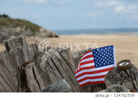Utah Beach WWII with Flag of USA and compass in sharp focus with beach and ocean in background. Sandy beach and fence posts. Normandy France rememberance of Veterans Day. High quality photo 114782559