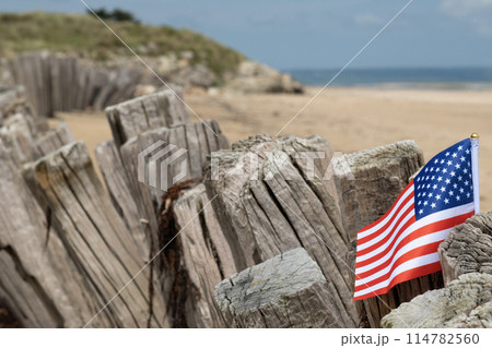 Utah Beach WWII with Flag of USA selective focus on flag. Sandy beach and fence posts. Normandy France rememberance of Veterans Day. High quality photo 114782560