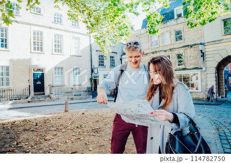 Fun, friends, travel and tourism concept. Young couple looking for direction during travel walk in old European city. Tourists consulting with a city guide map . Explore a new city together 114782750