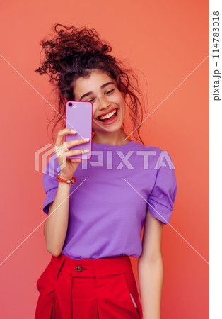 Happy young woman holding smartphone and smiling against an orange background 114783018
