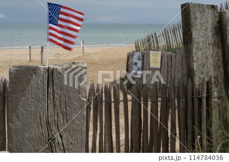 Utah Beach in Normandy, France. Mid range USA flag on wood sea fence, grass and sand dunes. Sunny sky light ble clouds. High quality photo Utah Beach in Normandy, France. Mid range USA flag on wood sea fence, grass and sand dunes. Sunny sky light ble clouds. High quality photo 114784036