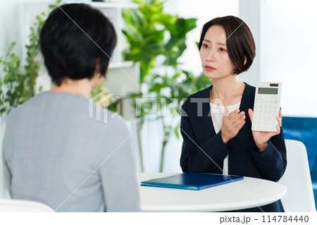 電卓を使って打ち合わせをするビジネスウーマン 114784440