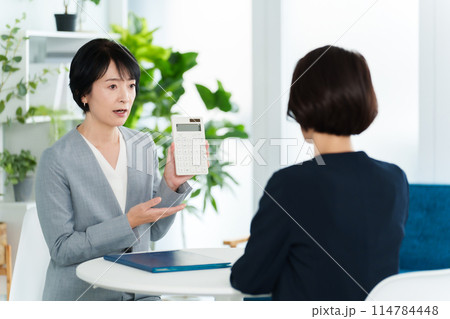 電卓を使って打ち合わせをするビジネスウーマン 電卓を使って打ち合わせをするビジネスウーマン 114784448