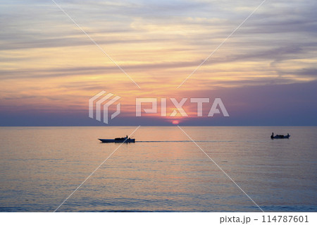 A half-disk of the sun and silhouettes of fishing boats at dawn in the United Arab Emirates 114787601