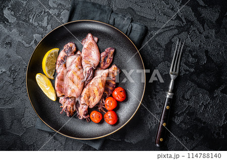 Seafood diner with grilled squid, calamary in a plate. Black background. Top view Seafood diner with grilled squid, calamary in a plate. Black background. Top view 114788140