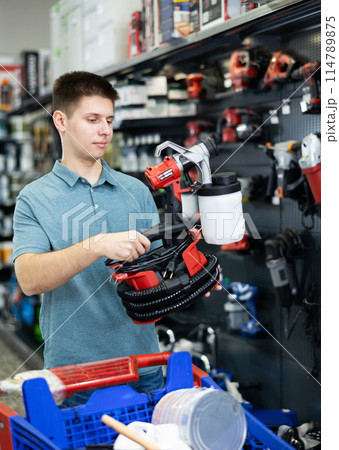 Young man involved in crafts or hobbies using of paint, choosing air sprayer in hardware store 114789875