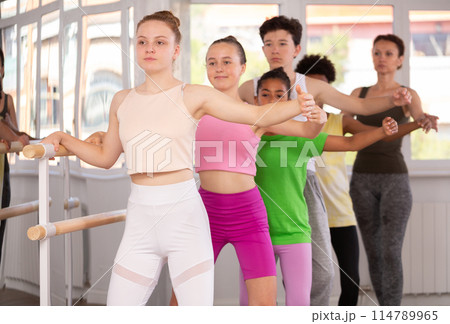 Teenage girl learning demi plie at barre with group of ballet students 114789965