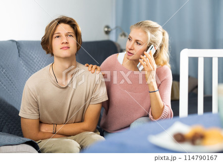 Woman sitting near her sad son and calling to doctor Woman sitting near her sad son and calling to doctor 114790167