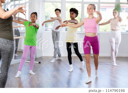 Positive teenage girl practicing ballet positions standing in row with others 114790198